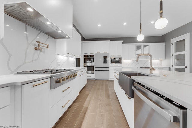 kitchen with exhaust hood, white cabinetry, appliances with stainless steel finishes, glass insert cabinets, and pendant lighting