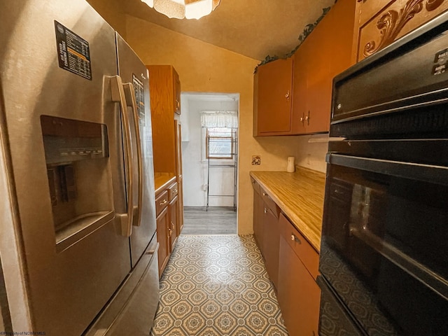 kitchen with lofted ceiling, stainless steel fridge with ice dispenser, and black oven