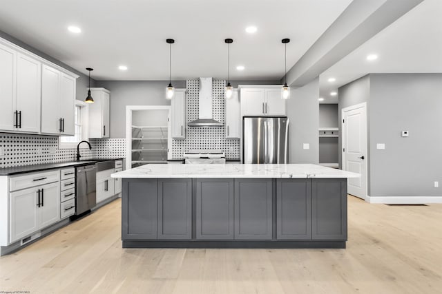 kitchen featuring pendant lighting, stainless steel appliances, a kitchen island, and wall chimney range hood