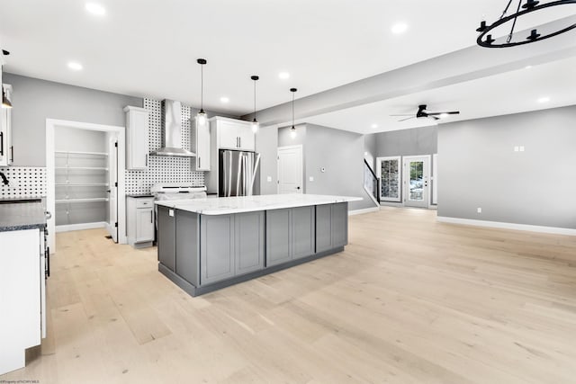 kitchen featuring white cabinetry, hanging light fixtures, stainless steel fridge, a kitchen island, and wall chimney range hood