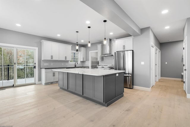 kitchen with stainless steel refrigerator, white cabinetry, hanging light fixtures, a kitchen island, and wall chimney exhaust hood