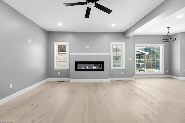 unfurnished living room featuring ceiling fan with notable chandelier and light hardwood / wood-style floors