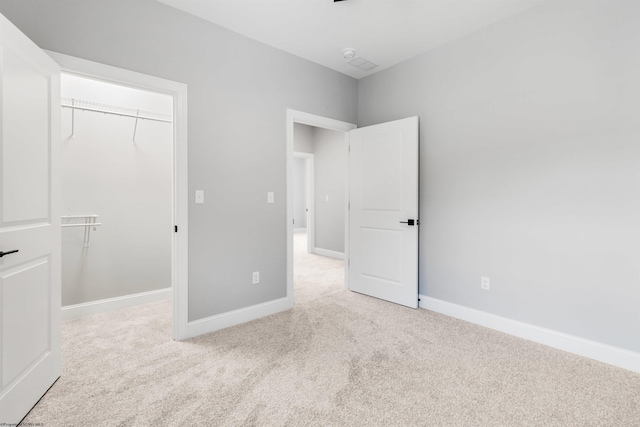 unfurnished bedroom featuring a spacious closet, light carpet, and a closet