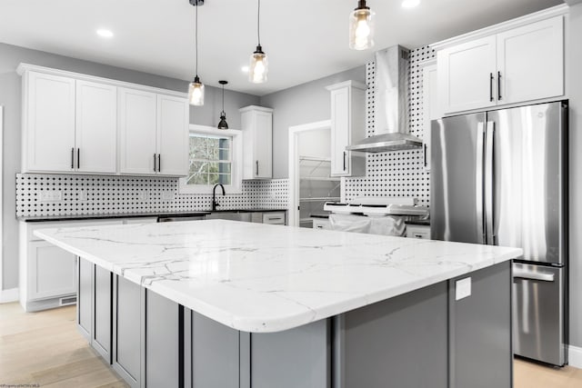 kitchen featuring pendant lighting, wall chimney range hood, stainless steel refrigerator, and a center island