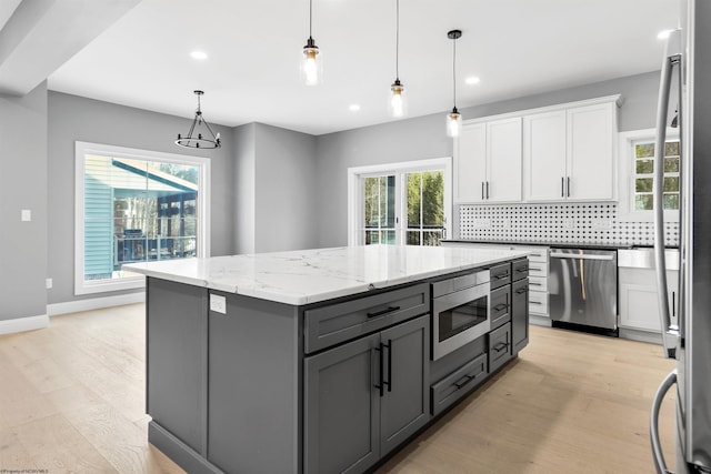 kitchen with appliances with stainless steel finishes, a center island, light stone counters, white cabinets, and decorative light fixtures