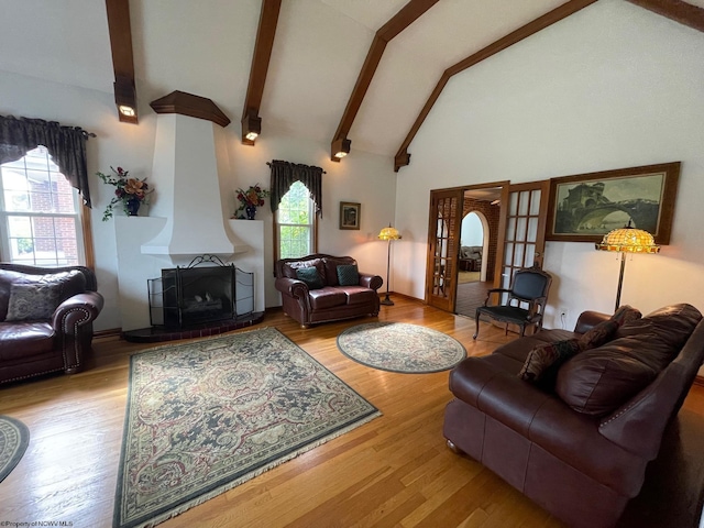 living room with beam ceiling, light wood-type flooring, a large fireplace, and high vaulted ceiling