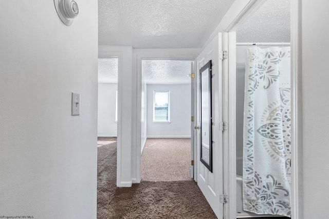 hall with a textured ceiling and dark colored carpet