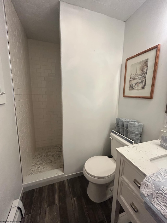 bathroom with a baseboard radiator, tiled shower, toilet, vanity, and hardwood / wood-style flooring