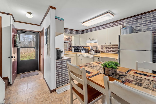 kitchen with sink, white cabinets, brick wall, white appliances, and light tile patterned flooring