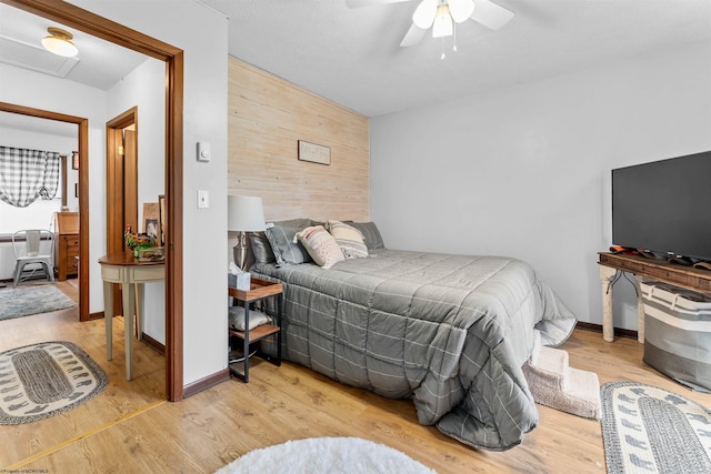 bedroom with ceiling fan, light hardwood / wood-style floors, and wooden walls