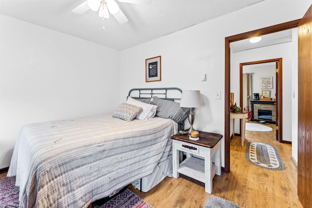 bedroom with a fireplace, wood-type flooring, and ceiling fan