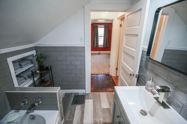 bathroom with a bathtub, vanity, hardwood / wood-style flooring, and tile walls