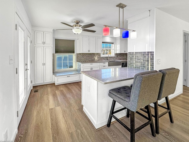 kitchen featuring light stone countertops, white cabinetry, hanging light fixtures, light hardwood / wood-style flooring, and decorative backsplash