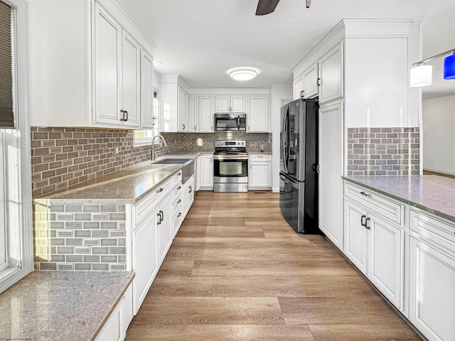 kitchen with decorative backsplash, appliances with stainless steel finishes, sink, white cabinets, and light hardwood / wood-style floors