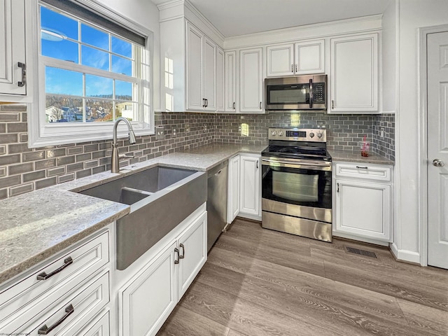 kitchen with light stone countertops, light wood-type flooring, backsplash, stainless steel appliances, and white cabinetry