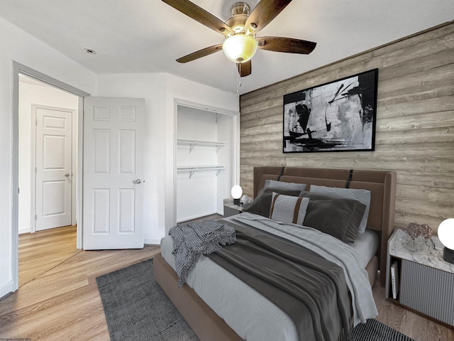 bedroom featuring ceiling fan, light wood-type flooring, wooden walls, and a closet