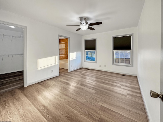 unfurnished bedroom with light hardwood / wood-style flooring, ensuite bath, ceiling fan, a spacious closet, and a closet