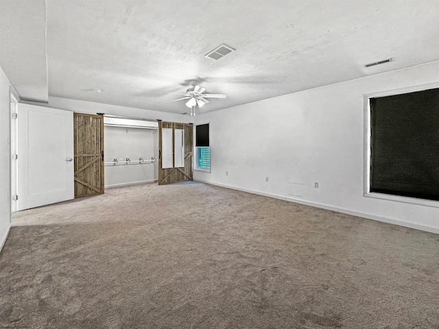 unfurnished bedroom featuring a textured ceiling, a barn door, carpet floors, and ceiling fan