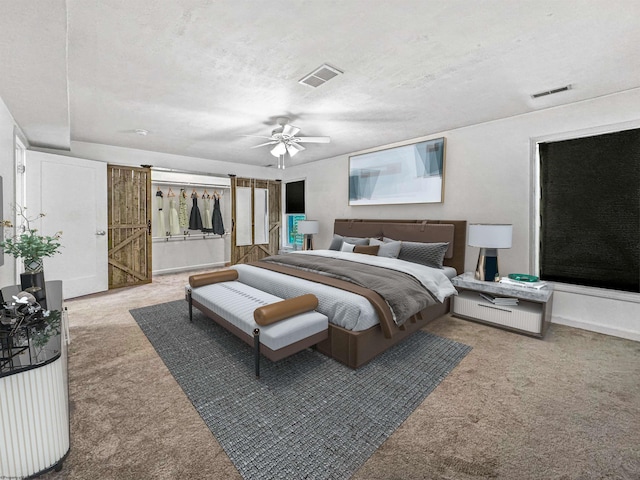 carpeted bedroom featuring a barn door, ceiling fan, and a textured ceiling