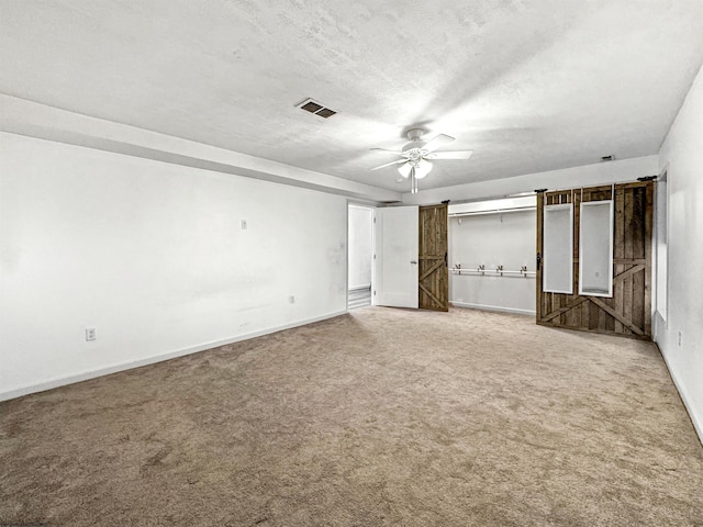 unfurnished bedroom with carpet flooring, ceiling fan, a barn door, and a textured ceiling