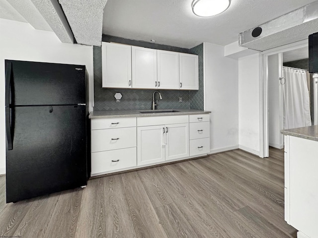 kitchen featuring decorative backsplash, black fridge, sink, light hardwood / wood-style flooring, and white cabinetry