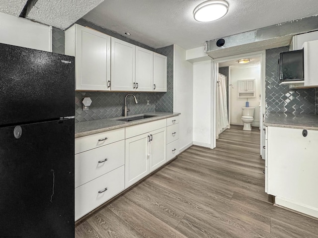 kitchen with black fridge, sink, white cabinets, and light wood-type flooring