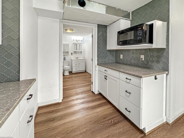 kitchen featuring decorative backsplash, white cabinetry, light hardwood / wood-style floors, and a textured ceiling