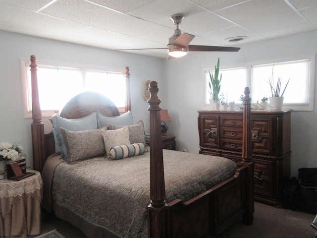 bedroom featuring ceiling fan, a drop ceiling, and multiple windows