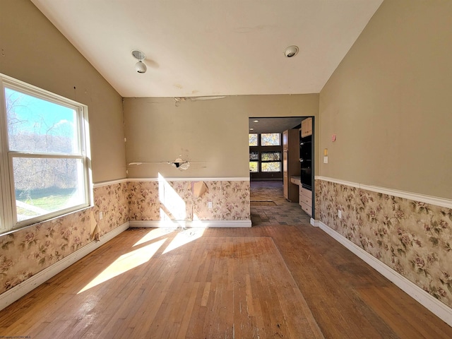 spare room featuring a wealth of natural light, wood-type flooring, and vaulted ceiling