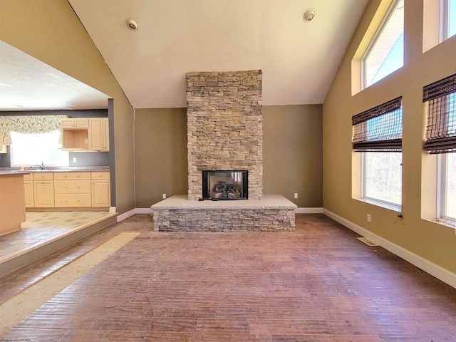 unfurnished living room with hardwood / wood-style floors, a stone fireplace, sink, and high vaulted ceiling