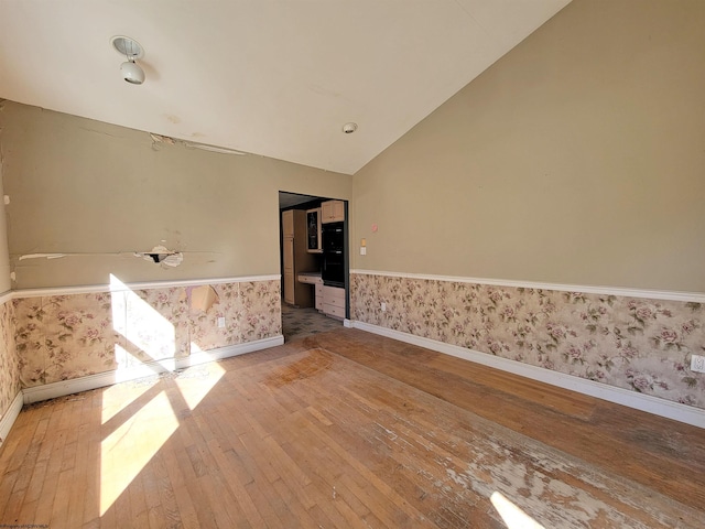 spare room with hardwood / wood-style floors and vaulted ceiling