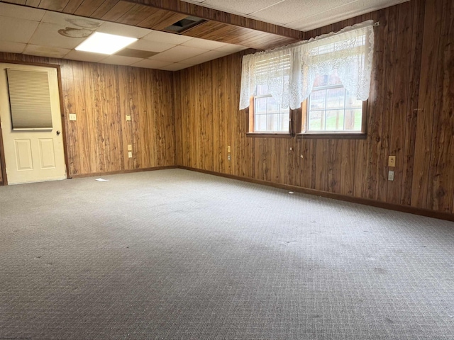 carpeted spare room featuring a paneled ceiling and wooden walls