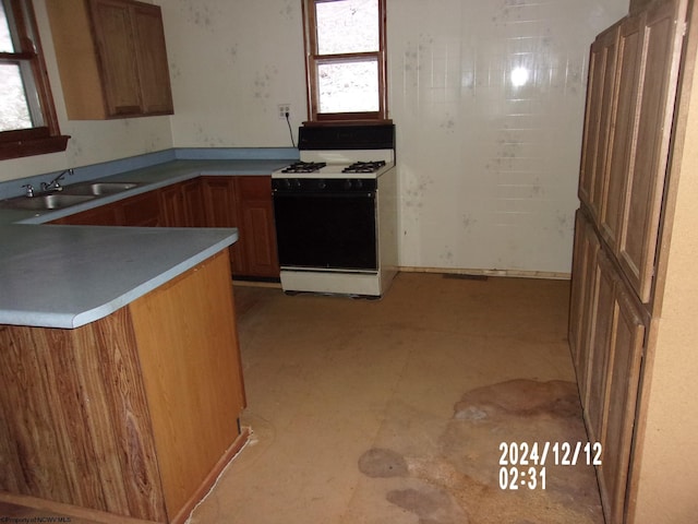 kitchen featuring kitchen peninsula, white gas range, and sink