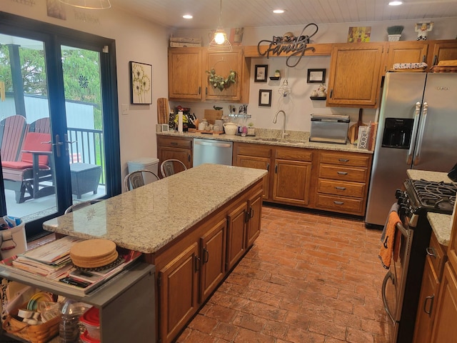 kitchen with decorative light fixtures, stainless steel appliances, light stone counters, and sink