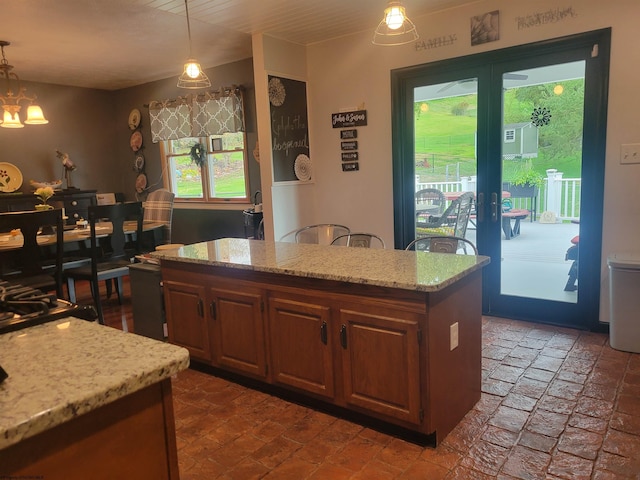 kitchen with a notable chandelier, a center island, light stone counters, and hanging light fixtures