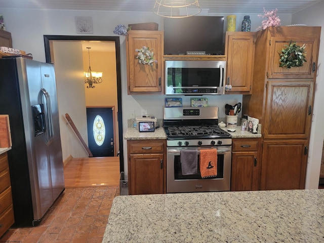 kitchen with appliances with stainless steel finishes, decorative light fixtures, an inviting chandelier, and light stone counters