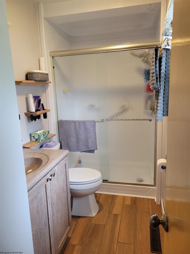 bathroom featuring vanity, toilet, wood-type flooring, and a shower with door