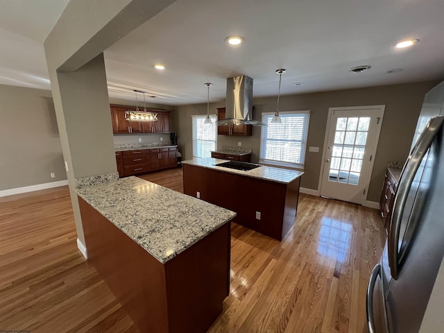 kitchen with hanging light fixtures, light hardwood / wood-style flooring, a kitchen island, island range hood, and stainless steel refrigerator