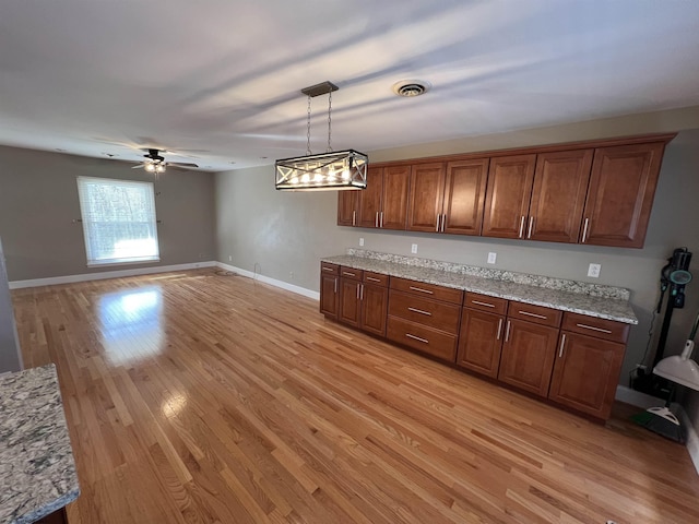 kitchen with ceiling fan, light hardwood / wood-style floors, light stone countertops, and hanging light fixtures