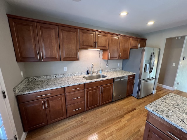 kitchen featuring light stone counters, sink, stainless steel appliances, and light wood-type flooring