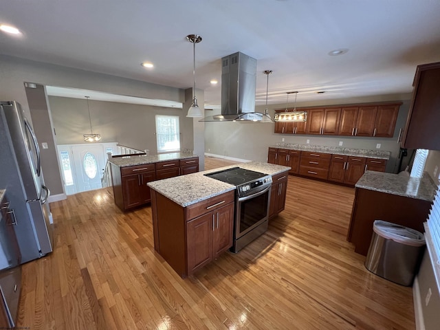 kitchen featuring island exhaust hood, appliances with stainless steel finishes, light wood-type flooring, a center island, and hanging light fixtures