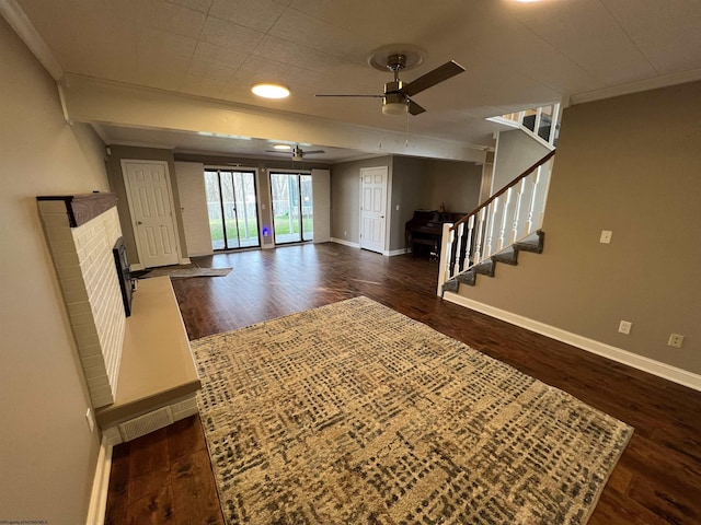 unfurnished living room featuring ceiling fan, dark hardwood / wood-style flooring, crown molding, and a brick fireplace