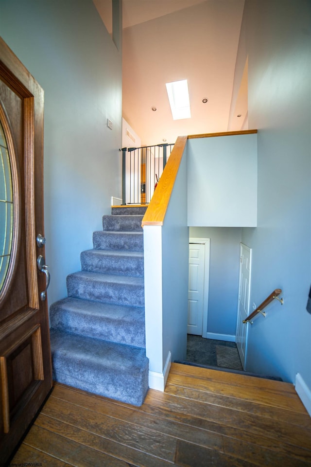 stairway with hardwood / wood-style floors, a skylight, and high vaulted ceiling