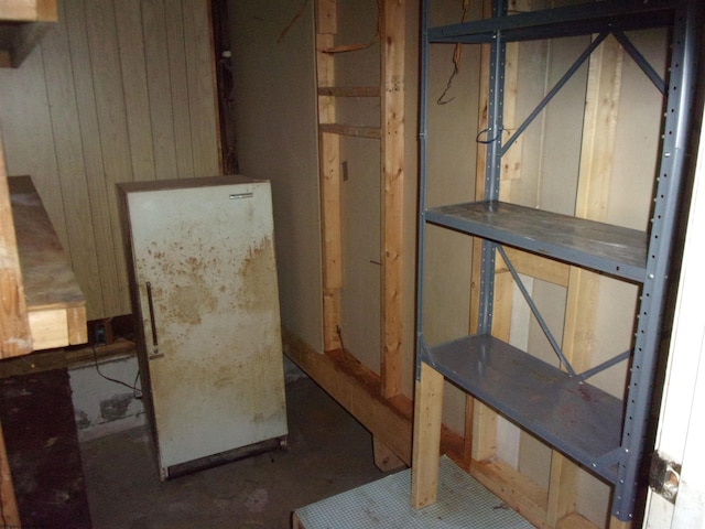 basement with white refrigerator and wooden walls