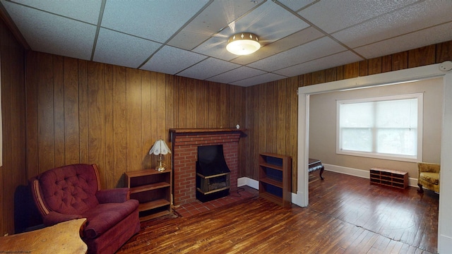 living area featuring dark hardwood / wood-style floors, wood walls, a drop ceiling, and a wood stove