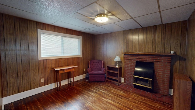 living area featuring hardwood / wood-style floors, a drop ceiling, a fireplace, and wooden walls