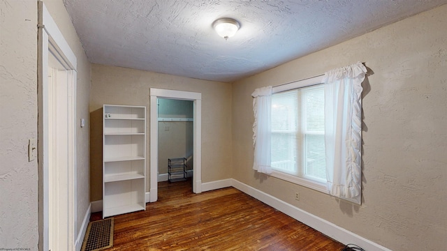unfurnished bedroom featuring wood finished floors, visible vents, a textured wall, and a textured ceiling