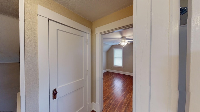 corridor with a textured ceiling, dark hardwood / wood-style flooring, and vaulted ceiling