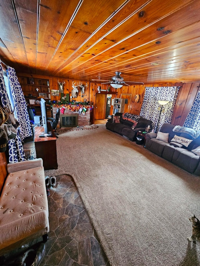 carpeted living room featuring ceiling fan, wood walls, wooden ceiling, and a brick fireplace