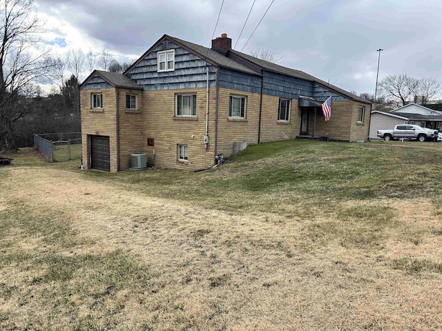 back of house featuring central AC unit, an attached garage, driveway, a lawn, and a chimney